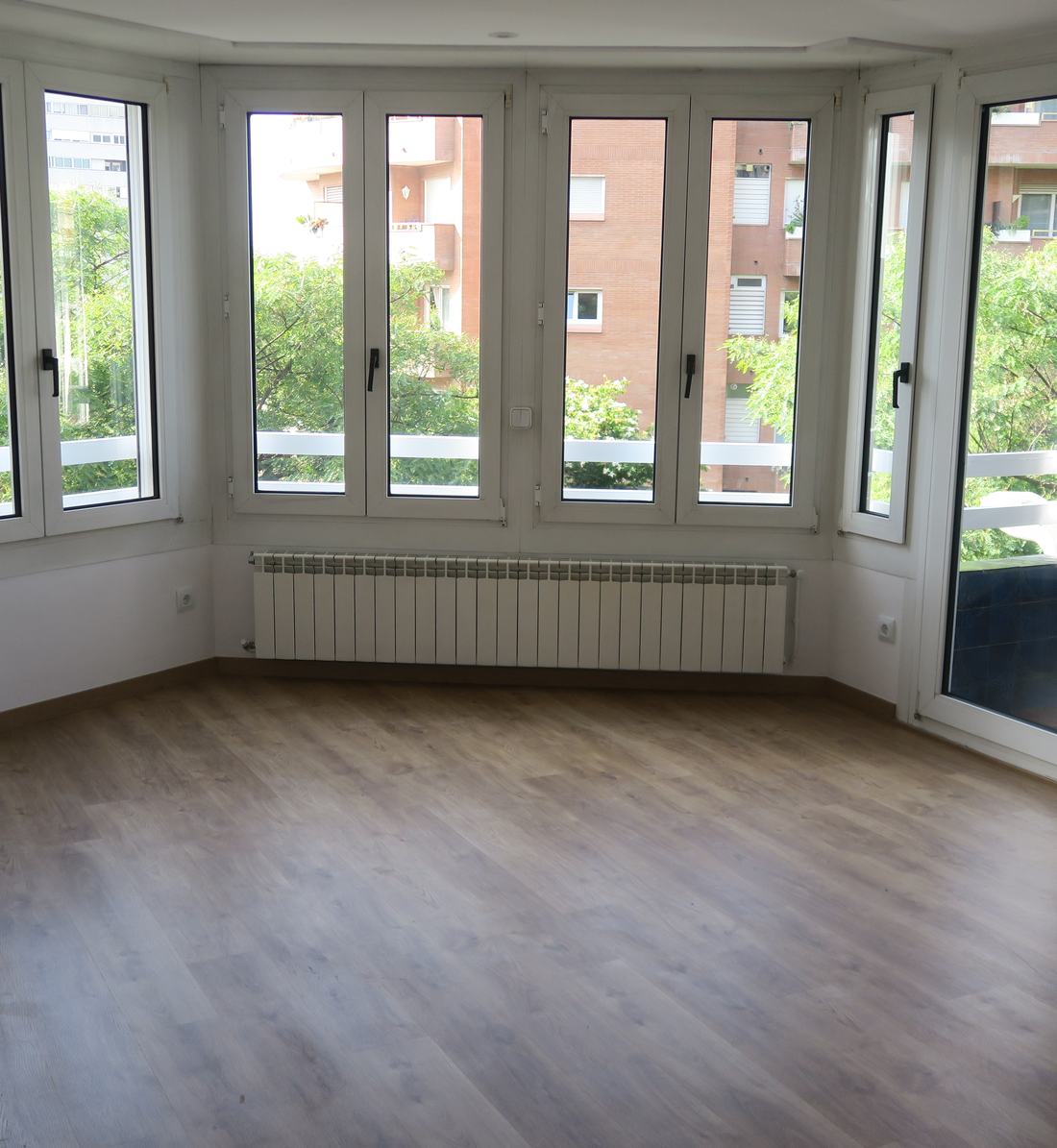Salón de un piso rehabilitado por Alphabitat, con suelo de madera y ventanales